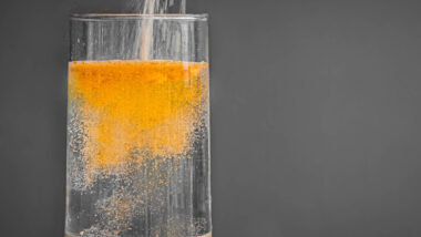 Powered orange drink mix being poured into a clear glass of water.