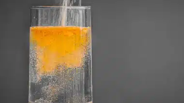 Powered orange drink mix being poured into a clear glass of water.