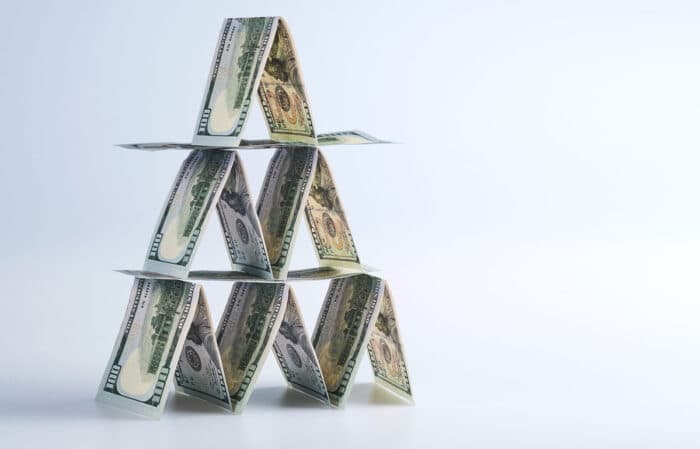 One hundred US dollar bills lined up in house of cards against a white background.