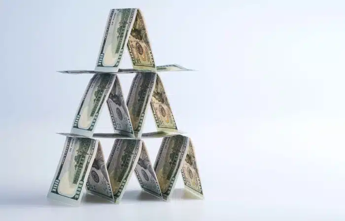 One hundred US dollar bills lined up in house of cards against a white background.