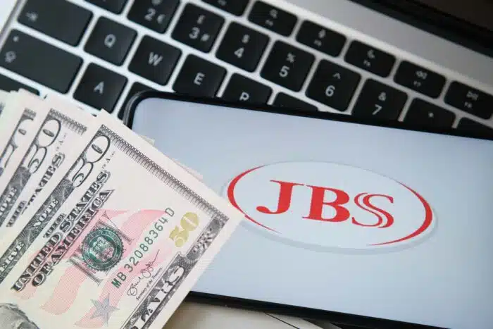 JBS USA meat producer logo seen on the smartphone screen with blurred money and laptop keyboard on the background - pork price fixing