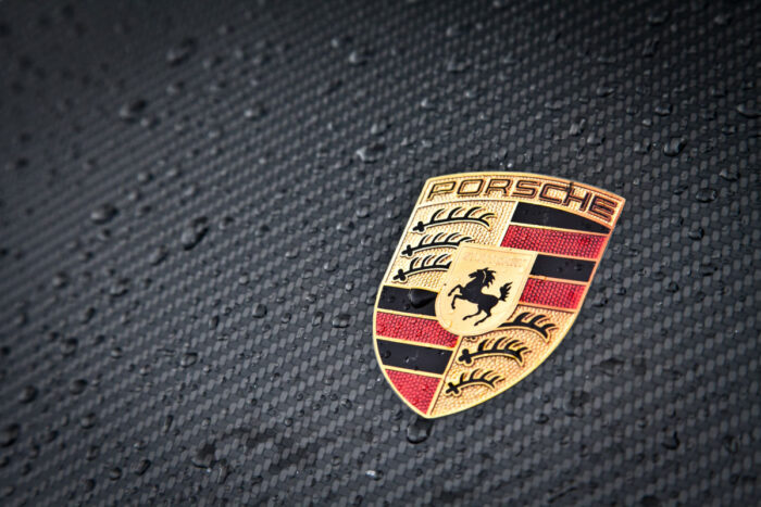 Close up of Porsche emblem against carbon fiber material.