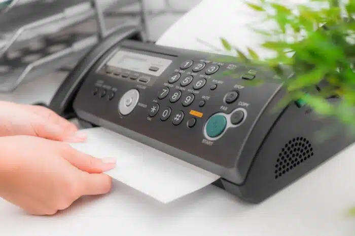 A person pulls a paper from a fax machine in an office - Best Doctors Settlement