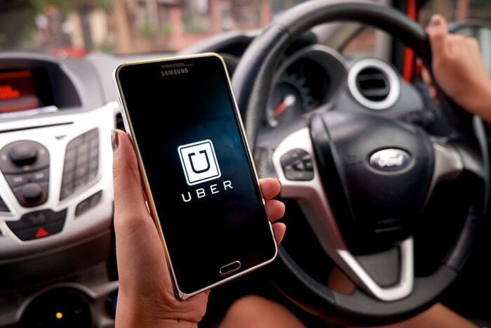 Woman's hand holding Uber app displayed on Samsung note 3 in car - Uber data breach