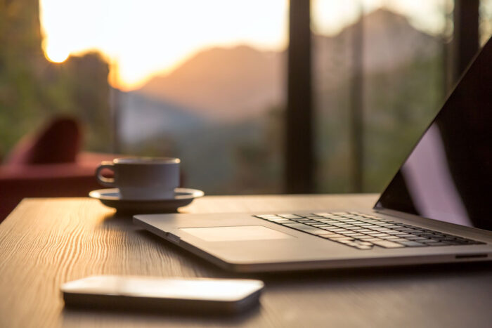 Nomad work Concept Image Computer Coffee Mug and Telephone large windows and sun rising, focus on laptop touch pad.