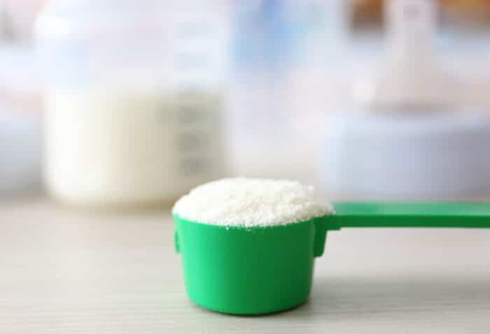 Baby milk formula in green spoon on wooden background.
