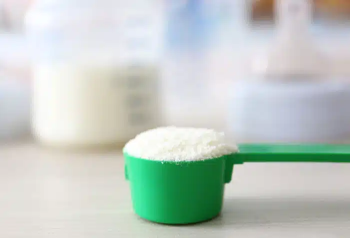 Baby milk formula in green spoon on wooden background.