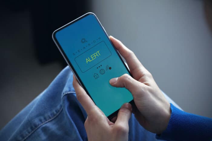 Close up of a persons hands using a smartphone, with an alert message displayed on the screen.