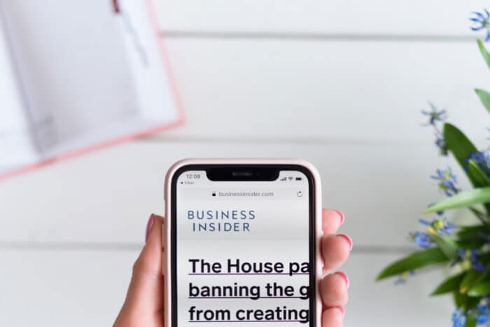 Woman holds Apple iPhone X with businessinsider.com site on the screen.