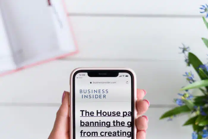 Woman holds Apple iPhone X with businessinsider.com site on the screen.