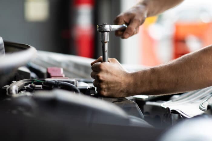 Close up of a mans hands using a tool to fix the engine of a car.
