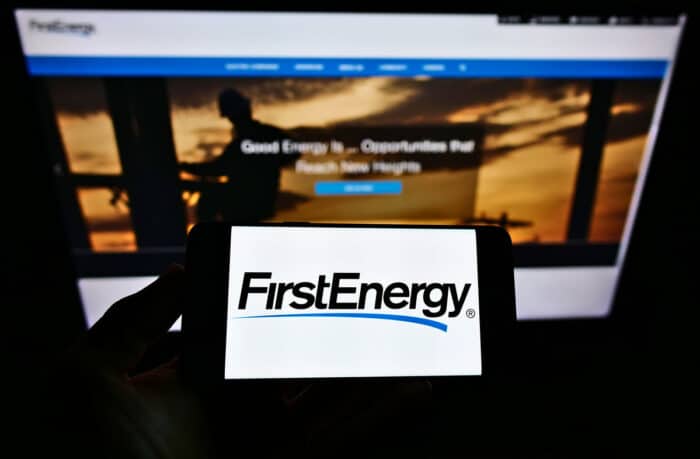 Person holding cellphone with business logo of US electric utility company FirstEnergy Corp. on screen in front of website.