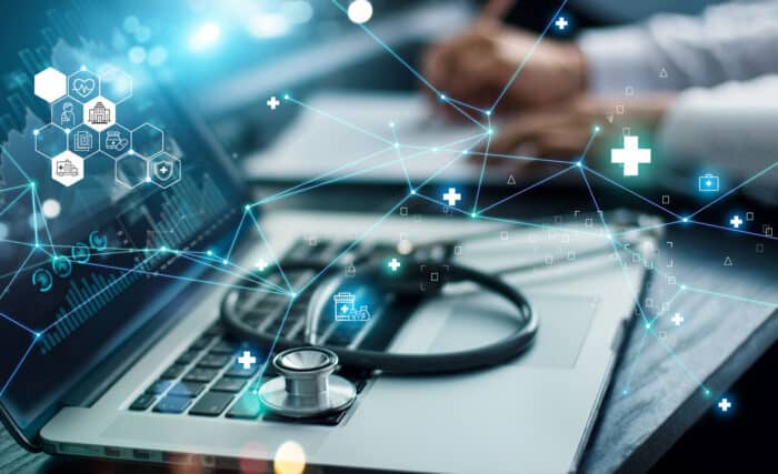 Close up of a stethoscope resting on an open laptop with a data overlay. Healthcare data breach concept.