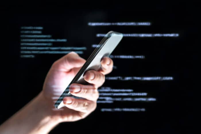 Close up of a hand holding a smartphone with a coding overlay. Spam text messaging concept.