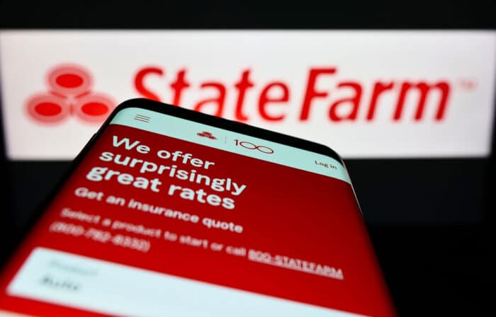 Mobile phone with webpage of US State Farm Mutual Automobile Insurance Company on screen in front of logo.