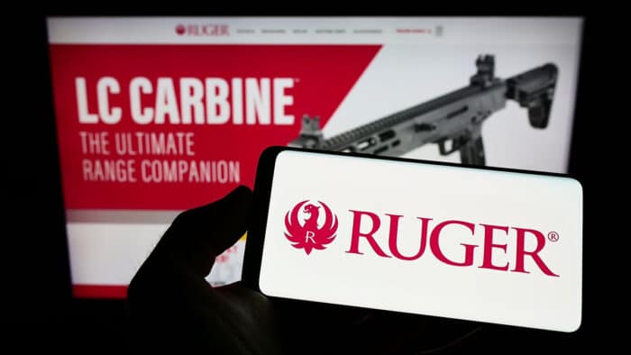 Person holding smartphone with logo of US company Sturm, Ruger and Company Inc. on screen in front of website.