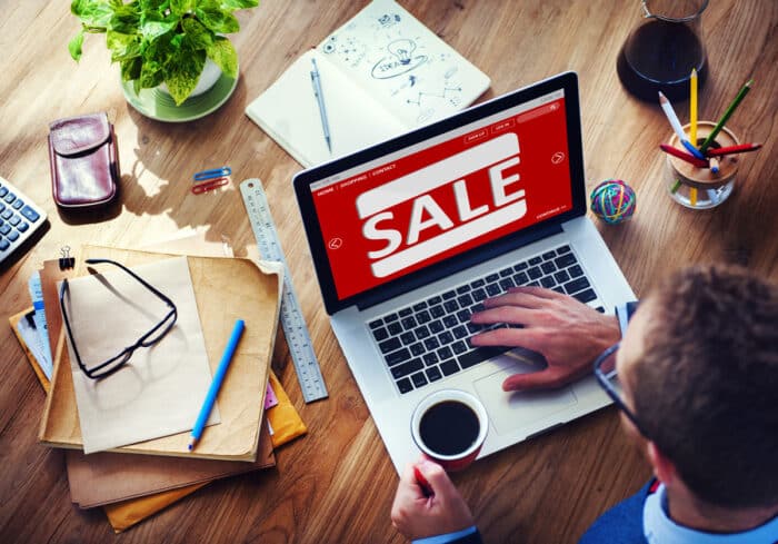 Man sitting at a desk, looking at his laptop that is showing a sale on screen. False advertising concept.