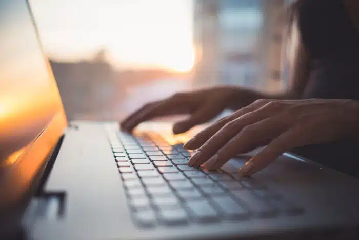 Close up of a womans hands typing on a laptop keyboard.