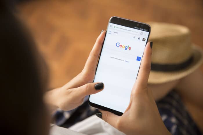 Young Women with black nail polish Open apps GOOGLE application on the screen on rustic brown wood background.