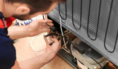 Male technician repairing refrigerator indoors.
