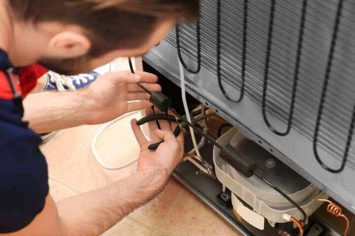 Male technician repairing refrigerator indoors.