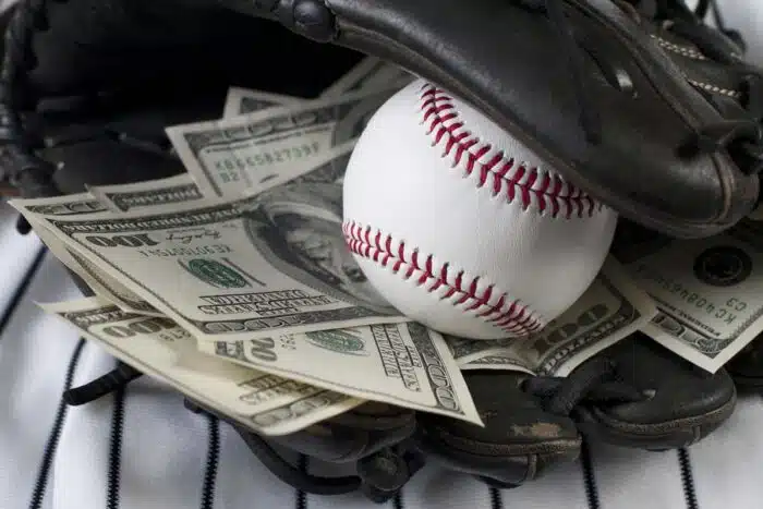 Close up of a baseball and money notes inside of a baseball mitt, representing the MLB settlement.