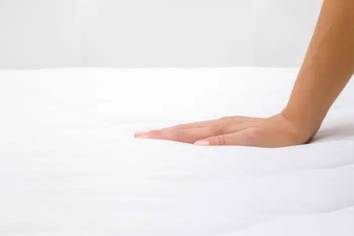 Close up of a woman's hand pressing on white mattress, representing the Mattress Firm Bed Tech lawsuit settlement.