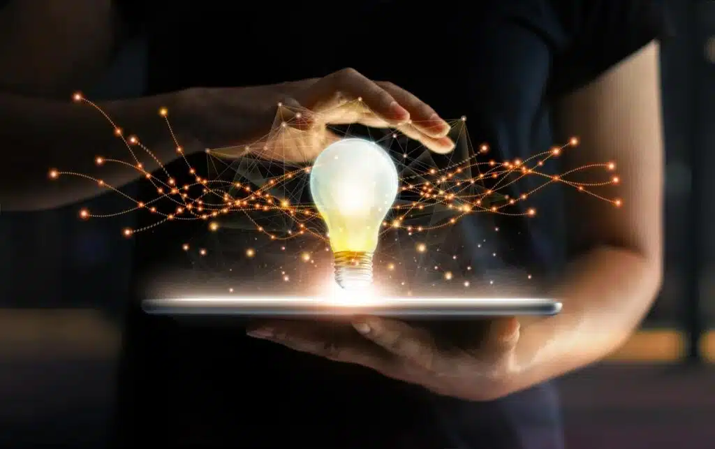 Hands holding tablet with light bulb future technologies and network connection on virtual interface background, representing the InventHelp class action settlement - Invention Submission Corp.
