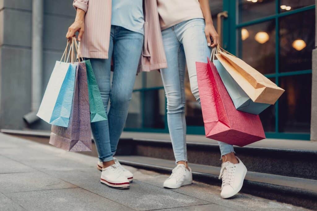 Cropped portrait of young lady and her mother holding colorful shopping bags.