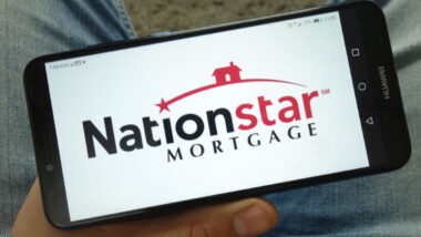 Man holding smartphone with Nationstar Mortgage Holdings Inc. logo displayed on screen.