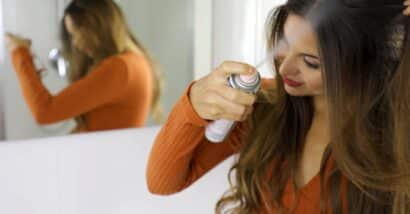 Young woman applying dry shampoo on her hair.
