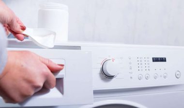Close up of a womans hands putting laundry detergent in a washer.