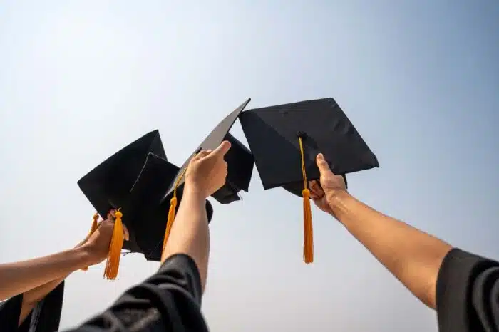 Close up of various college students hand holding their graduation cap in the air against the blue sky - ADA accessibility