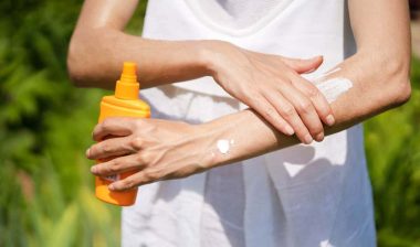 A young girl in a white summer dress applies sunscreen gel to her arms and shoulders.