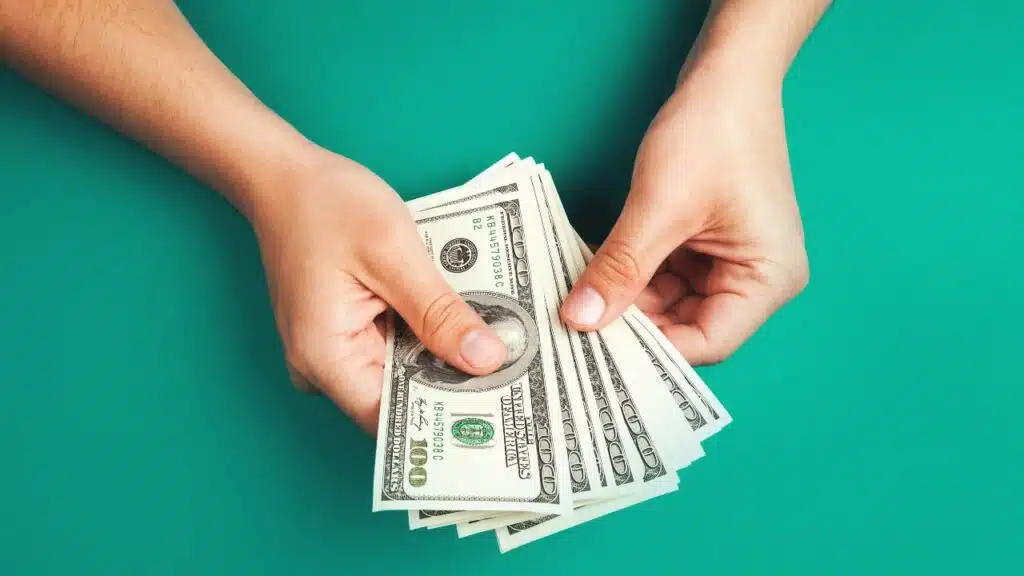 Hands holding a stack of 100 dollar bills, , representing settlement payments in the mail.