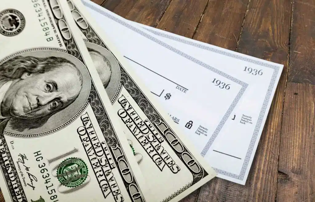 Close up of paper checks and cash against a wood background, caravan foods settlement.