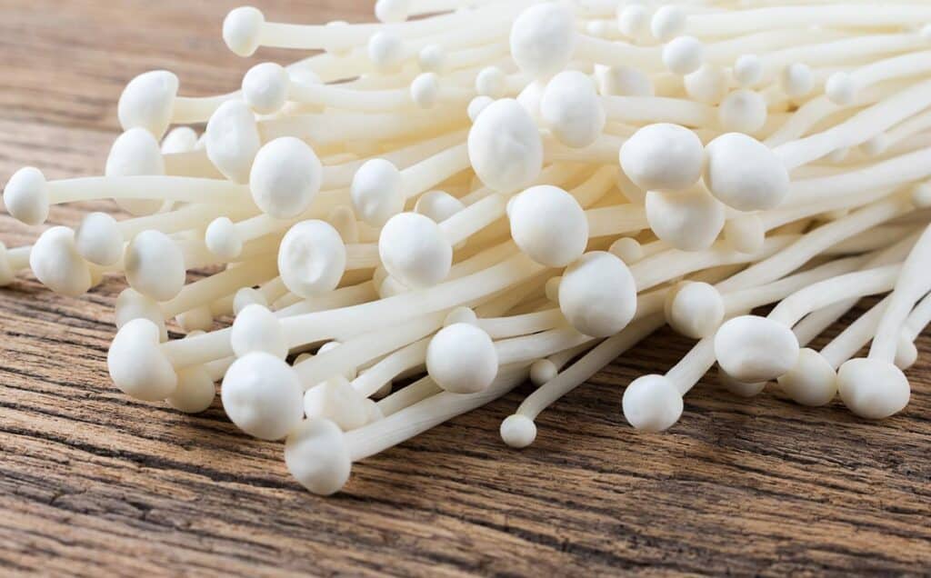 Close up of Enoki mushrooms on a wood surface.