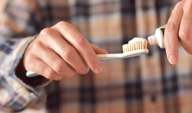 Close up of a mans hands putting toothpaste on a toothbrush.