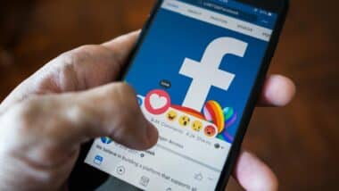 Close up of a person using a smartphone to react to a post on Facebook.