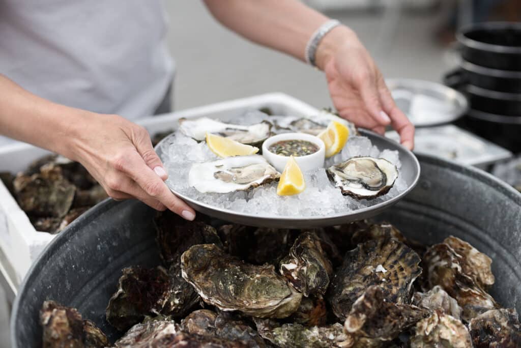 Close Up of Server with Tray of Fresh Shucked Oysters with Lemon Wedges.