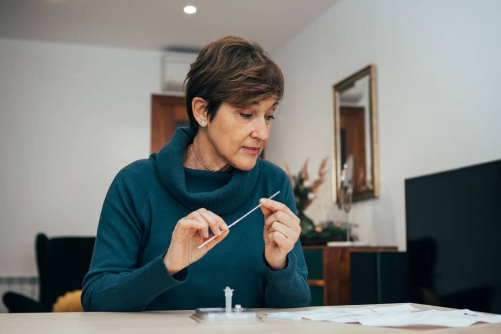 Senior woman sitting at home, studying the instructions for a self test for COVID-19.