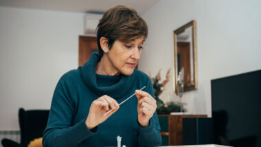 Senior woman sitting at home, studying the instructions for a self test for COVID-19.