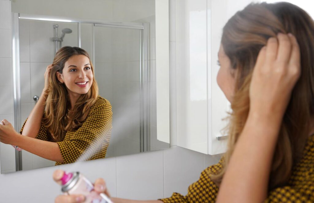 Young woman applying dry shampoo on her hair before going out.