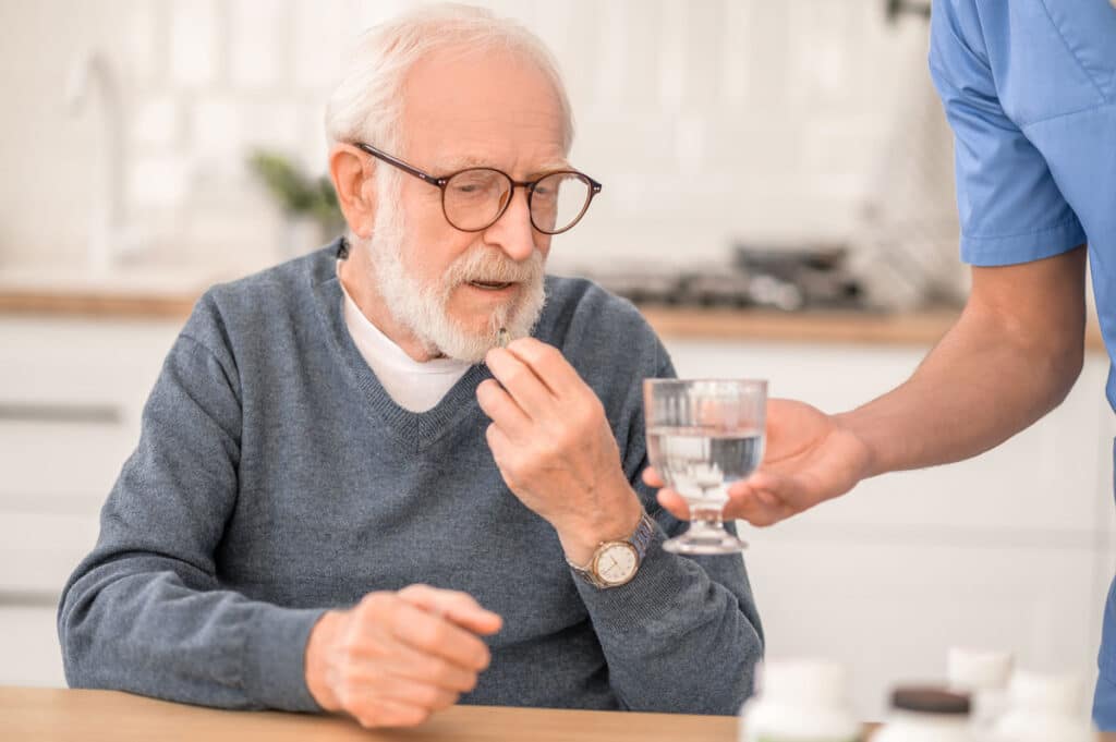 Elderly man taking a medicine under the supervision of his nurse, representing the Namenda class action lawsuit settlement.