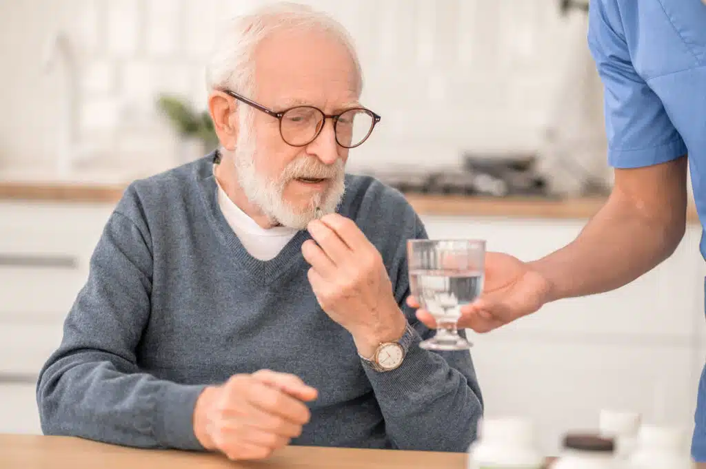 Elderly man taking a medicine under the supervision of his nurse, representing the Namenda class action lawsuit settlement.