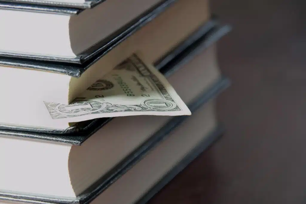 A single dollar bill in between books, representing the Monmouth University tuition settlement.