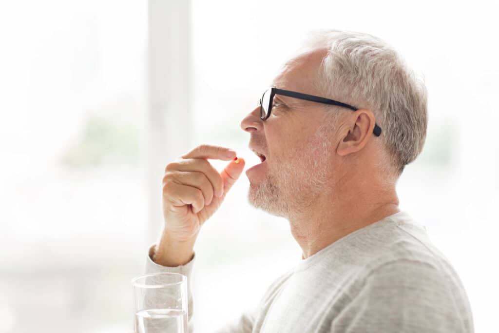 Elderly man taking a prescription pill.