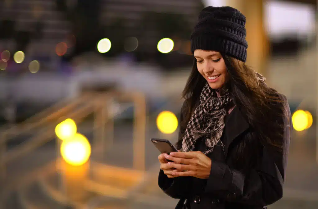 A woman in the city using her smartphone to order a ride using a rideshare app.