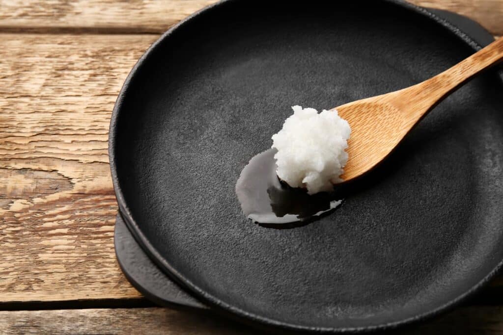 Spoon with coconut oil in frying pan on wooden table, representing the Barlean’s Organic Oils coconut oil class action lawsuit settlement.