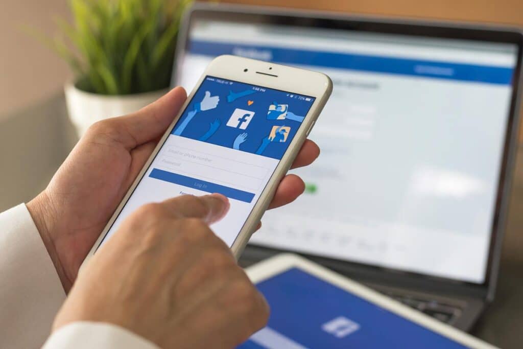 Close up of a persons hand holding a smart phone with Facebook website displayed on the screen.